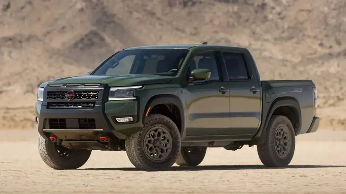 Зелёный пикап Nissan Frontier с двойной кабиной и внедорожными шинами стоит на сухом песчаном грунте у холмов