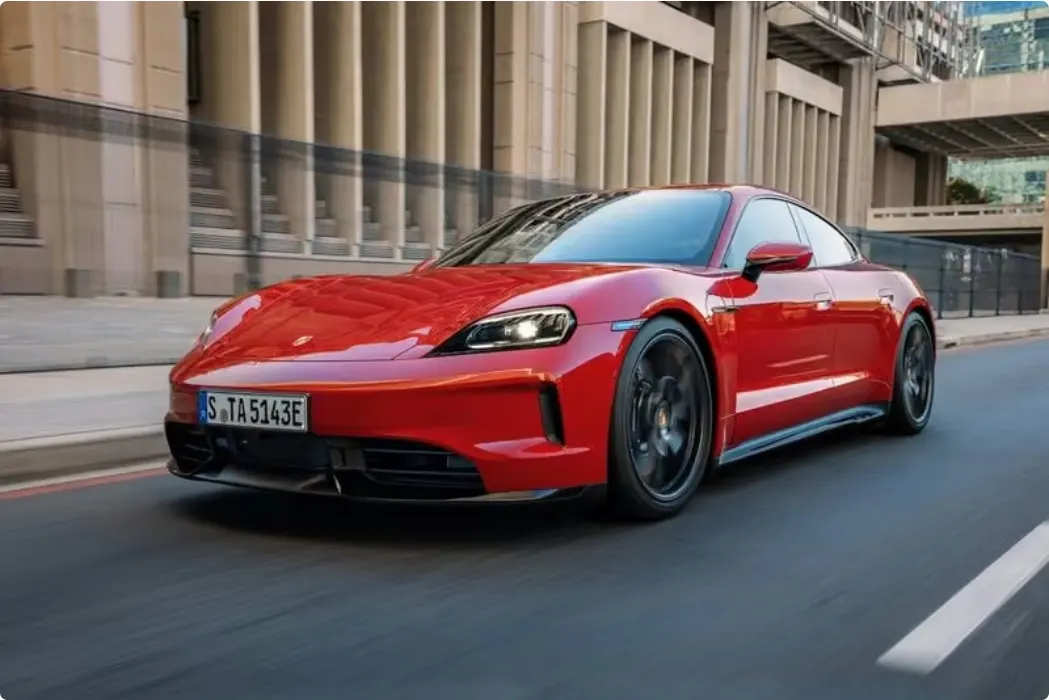 Красный Porsche Taycan на городской улице, вид спереди и сбоку: автомобиль в движении, на заднем плане здания