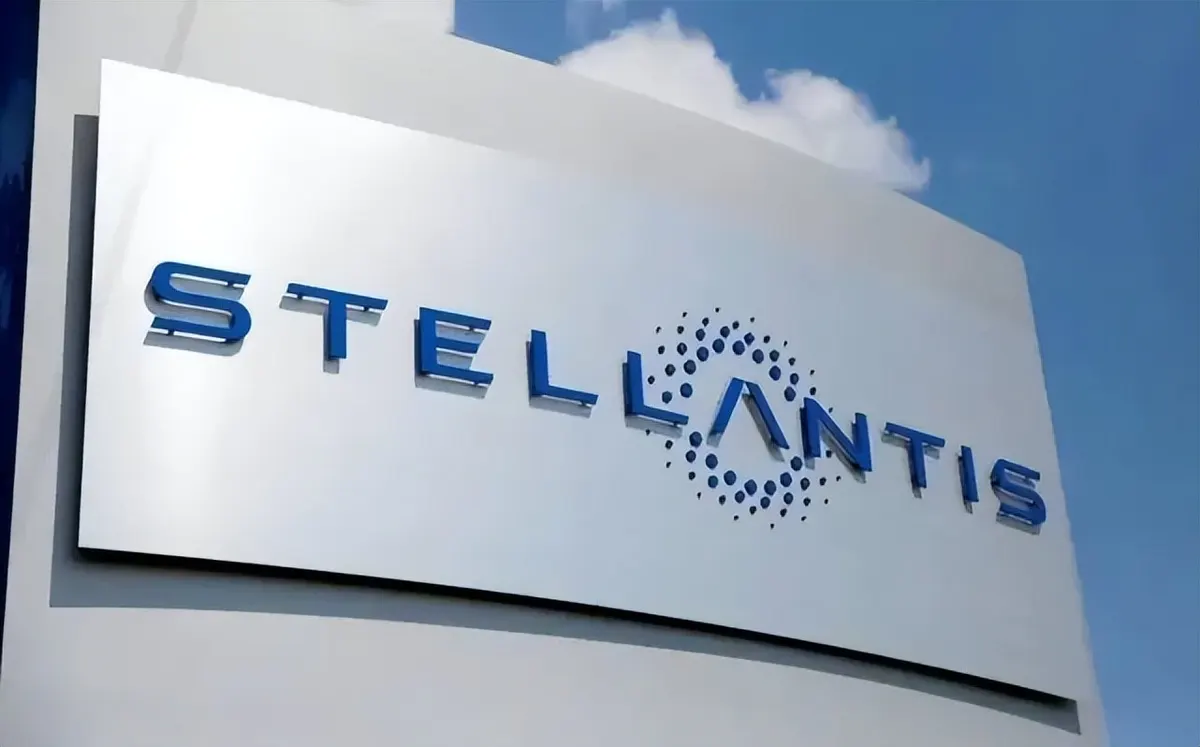 Синий логотип и надпись Stellantis на серебристом фирменном стенде на фоне неба с облаком