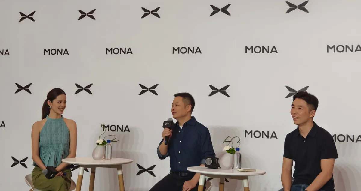 Три человека на сцене с микрофонами на фоне стены с логотипами Xpeng и надписью MONA