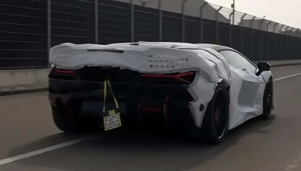 Прототип Lamborghini Revuelto SV с белым камуфляжем сзади на трассе у высокого ограждения