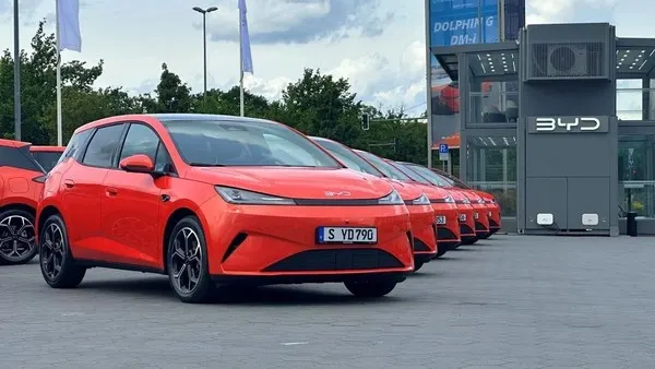Ряд оранжевых компактных электромобилей на площадке у автосалона в солнечную погоду