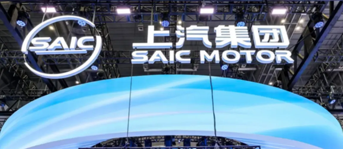 Объёмный логотип SAIC Motor над голубой изогнутой светодиодной конструкцией на выставочном стенде под фермами с софитами