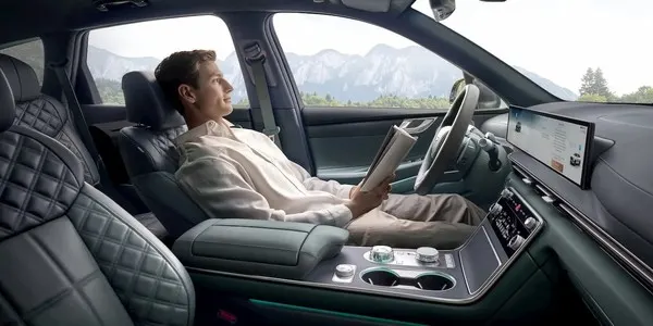 Мужчина читает журнал на переднем сиденье салона Genesis GV80, рядом широкий дисплей и центральный тоннель