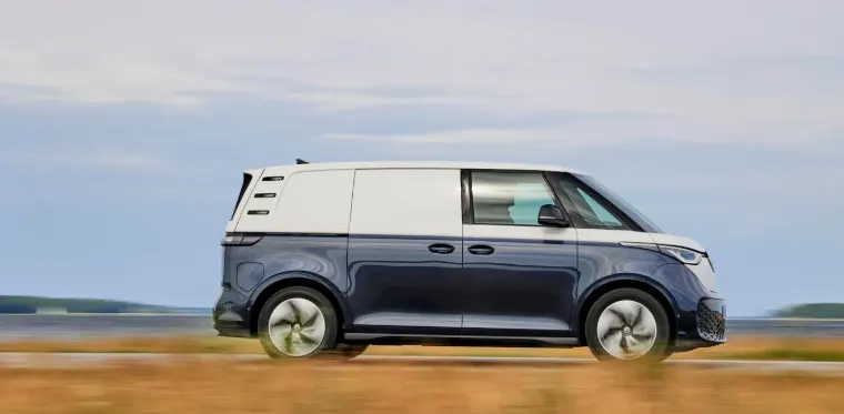Электрофургон Volkswagen ID. Buzz Cargo сине-белого цвета едет по дороге у воды, вид сбоку