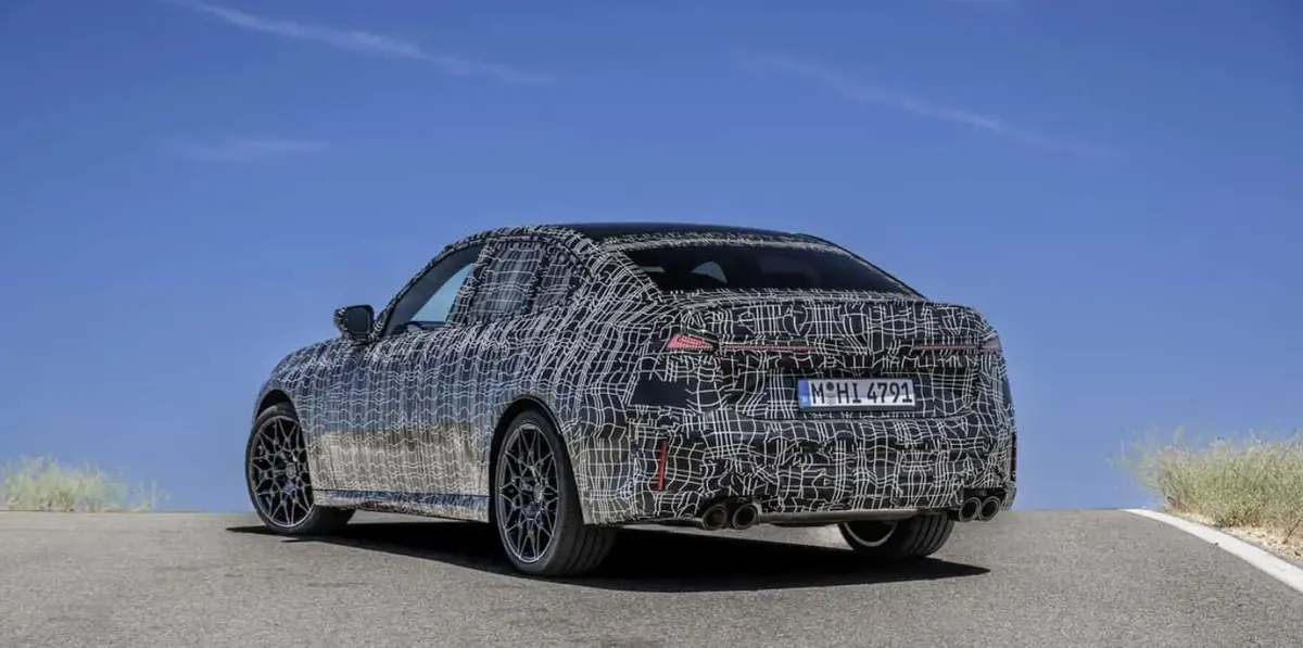 BMW 3 Series (G50) в камуфляже сзади: четыре выхлопные трубы, тёмные литые диски, синее небо