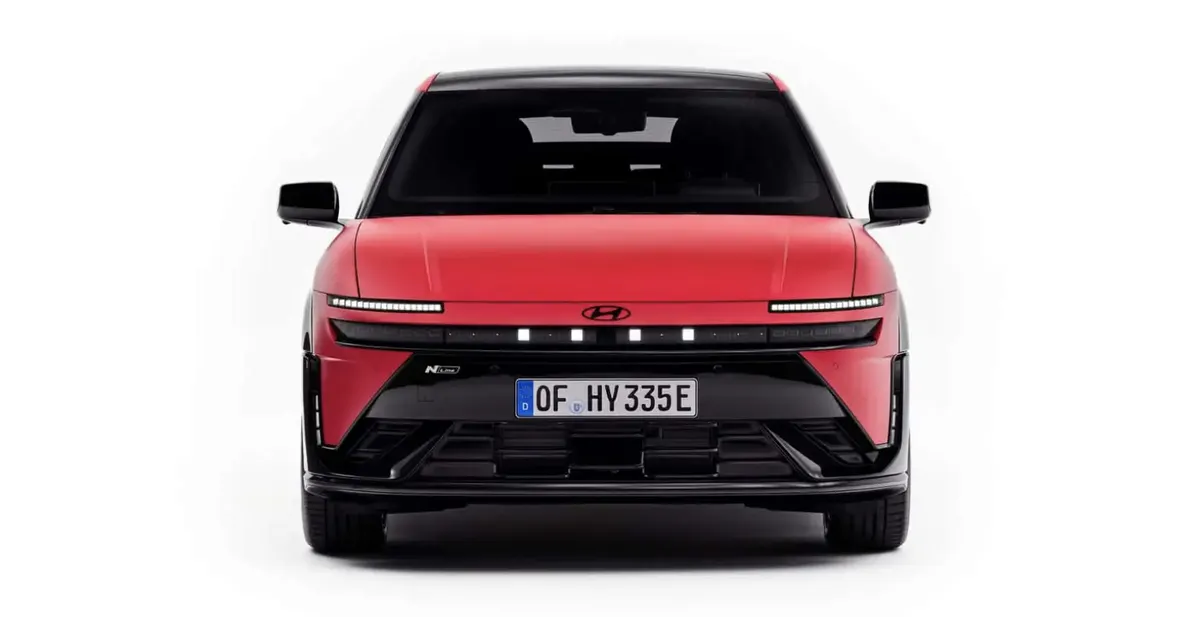 Красный электрокроссовер Hyundai спереди с чёрной крышей, узкими светодиодными фарами и немецким номером на белом фоне